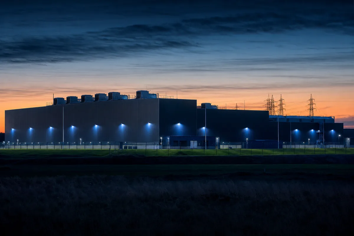 A hyperscale data centre exterior at dusk with cooling plant and transmission lines
